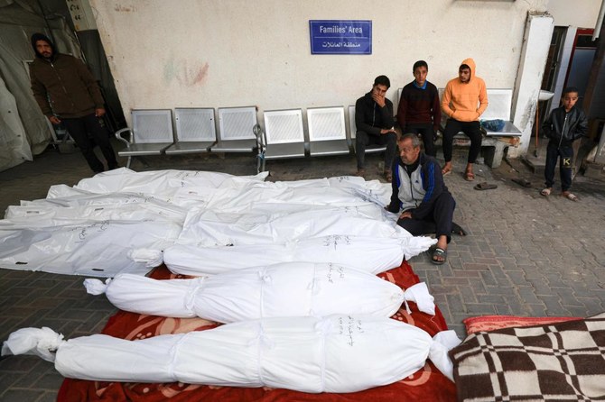 A Palestinian man sits beside shrouded corpses lined up at the al-Najjar hospital, following Israeli bombing on Rafah in the southern Gaza Strip on December 9, 2023, amid continuing battles between Israel and the militant group Hamas. (AFP)