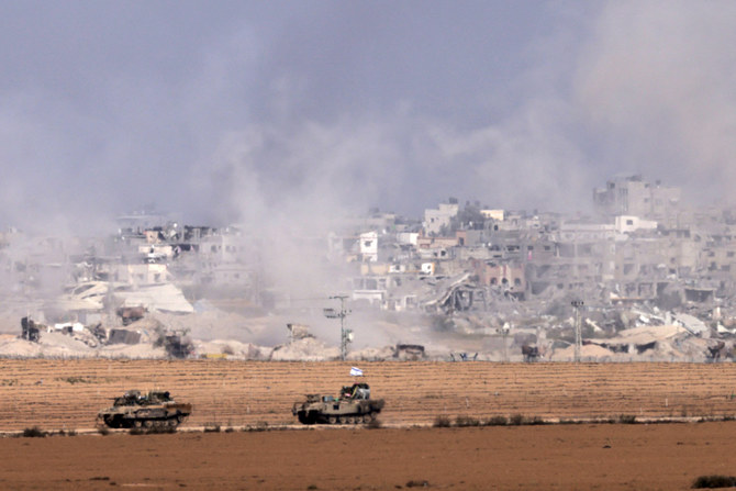 A picture taken from southern Israel near the border with the Gaza Strip on Dec. 10, 2023, shows Israeli armored personnel carriers driving along the border fence as smoke rises above the Palestinian enclave amid ongoing battles with the Palestinian Hamas militant group. (AFP)