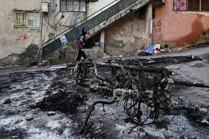 Palestinians walk past a burnt motorcycle following a three-day incursion by the Israeli army on the Jenin camp in the occupied West Bank bank city of Jenin on December 14, 2023. (AFP)