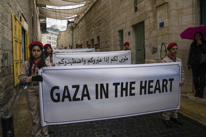 Palestinian scouts hold signs in solidarity with Palestinians in the Gaza Strip calling to end the Israel-Hamas war, near the Church of the Nativity, traditionally believed to be the birthplace of Jesus, on Christmas Eve in the West Bank city of Bethlehem, Sunday, Dec. 24, 2023. (AP)