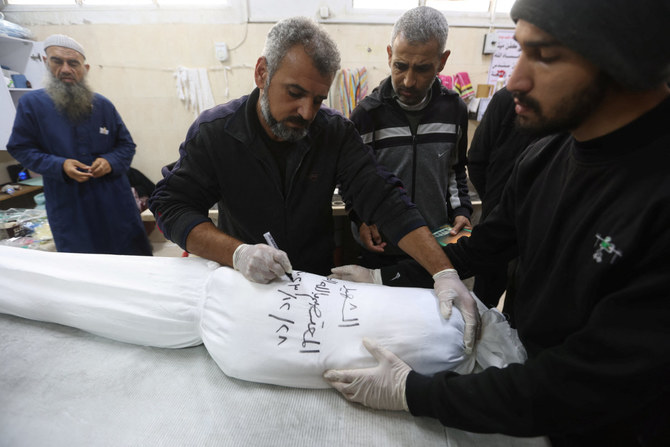 Mohammed Abu Mussa, a volunteer at Keratan society which prepares dead bodies for burial, writes the name and date on a white shroud covering the body of a Palestinian killed in an Israeli strike at a hospital in Rafah, southern Gaza Strip, on Dec. 28, 2023. (REUTERS/Ibraheem Abu Mustafa)