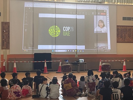 A group of children sitting in a room with a large projector screen