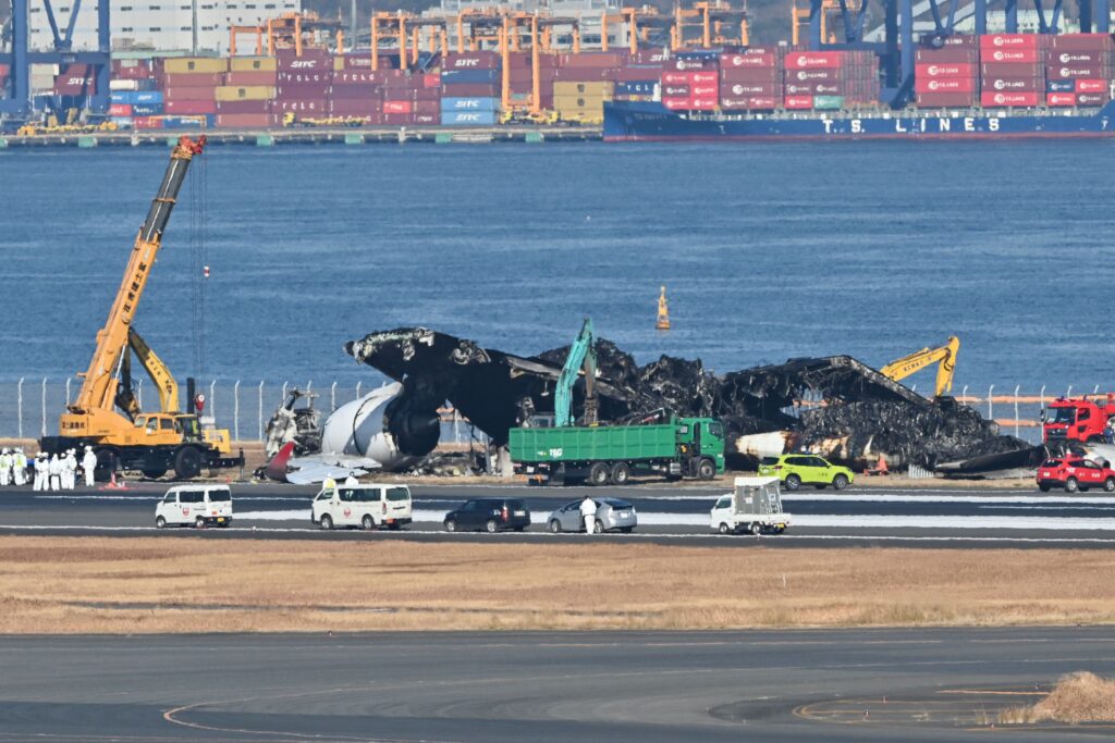 Officials begin to remove the remaining debris of a Japan Airlines (JAL) passenger plane from the runway area at Tokyo International Airport at Haneda on January 5, 2024, three days after the JAL airliner hit a smaller coast guard plane on the ground. Five of the six people on the smaller aircraft died but all 379 people onboard the Japan Airlines Airbus were evacuated just before it was engulfed in flames. (Photo by Richard A. BROOKS / AFP)