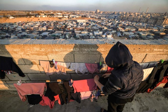 A boy lays wet clothes to dry on a laundry line atop a rooftop overlooking the tent camps of displaced Palestinians in Rafah in the southern Gaza Strip close to the border with Egypt on Dec. 31, 2023. (AFP)