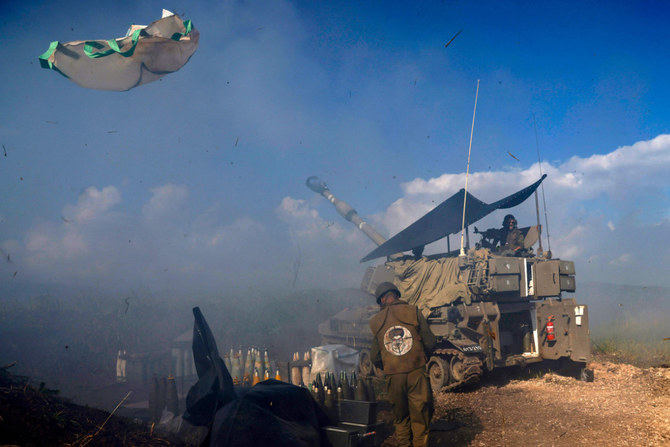 An Israeli soldier, wearing a patch on the back of his flack jacket showing Hezbollah leader Hassan Nasrallah as a target, stands in front of a tank in Upper Galilee in northern Israel, as an artillery unit shells southern Lebanon on January 4, 2024. (AFP)