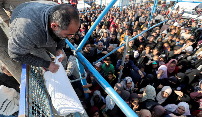 A Palestinian man holds a flour bag as others wait to receive theirs from the United Nations Relief and Works Agency (UNRWA) during a temporary truce between Hamas and Israel, in Khan Younis in the southern Gaza Strip, November 29, 2023. (REUTERS)