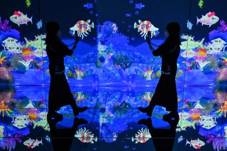 A woman is reflected as she takes photos of artwork drawn by visitors during a tour of the new location for the digital art of Japanese collective
