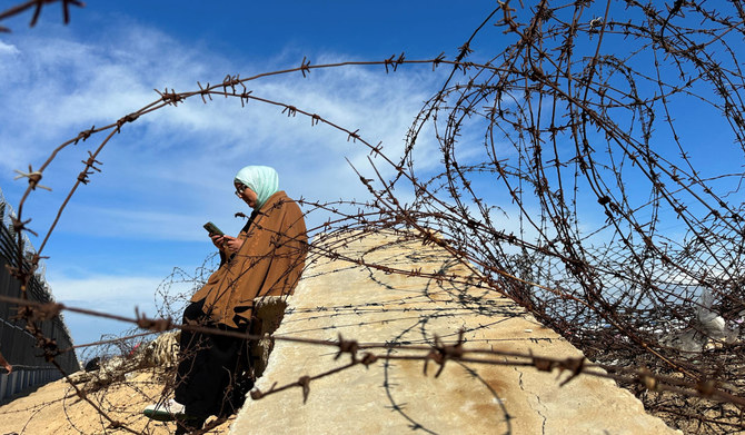 A displaced Palestinian woman tries to get internet service on her phone through the Egyptian networks to communicate with her relatives, near the border with Egypt, in Rafah in the southern Gaza Strip February 1, 2024. (REUTERS)