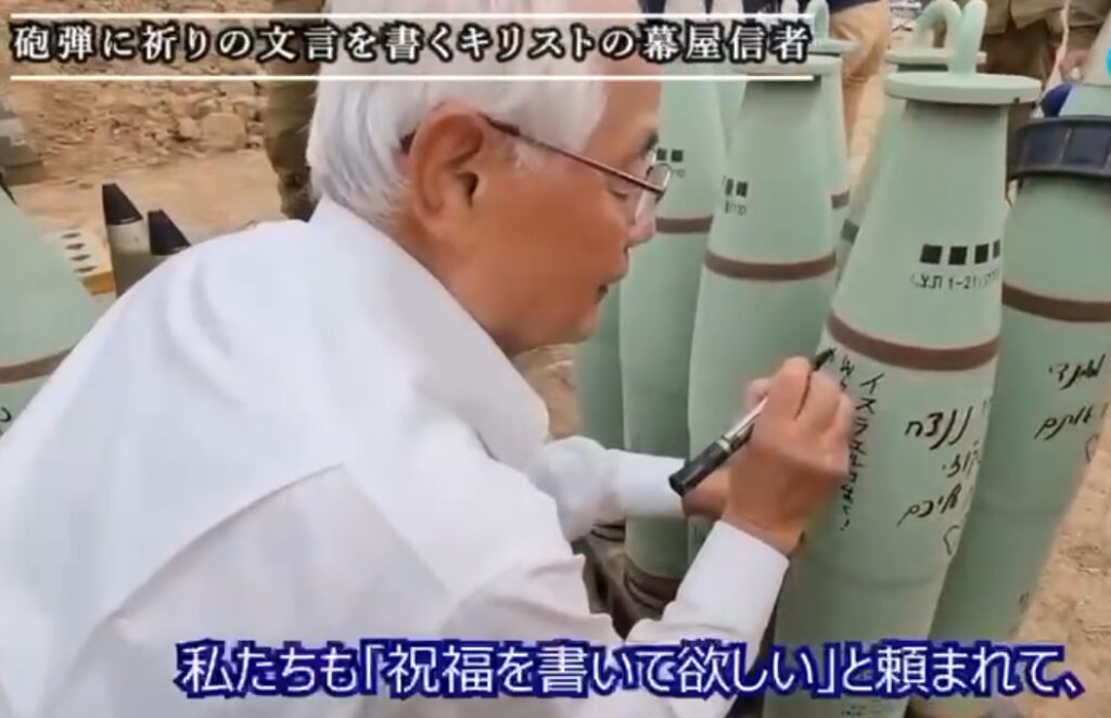 A member of the pro-Israel Japanese Mukaya cult is seen at an Israeli military occupation base signing “blessings” and “prayers” on bombs prepared to hit Gaza. The Japanese words on the photo say: “We were asked to write a blessing,” and “Believers in the Tabernacle of Christ write prayer words on bombs.”(Mukaya website) 