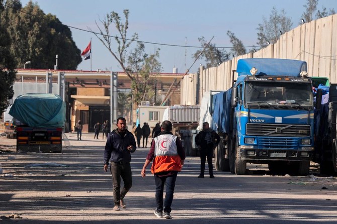 People walk past trucks carrying humanitarian aid that entered Gaza by truck through the Kerem Shalom (Karm Abu Salem) border crossing in the southern part of the Palestinian territory on Feb. 17, 2024, as they wait to be unloaded in Rafah. (AFP)