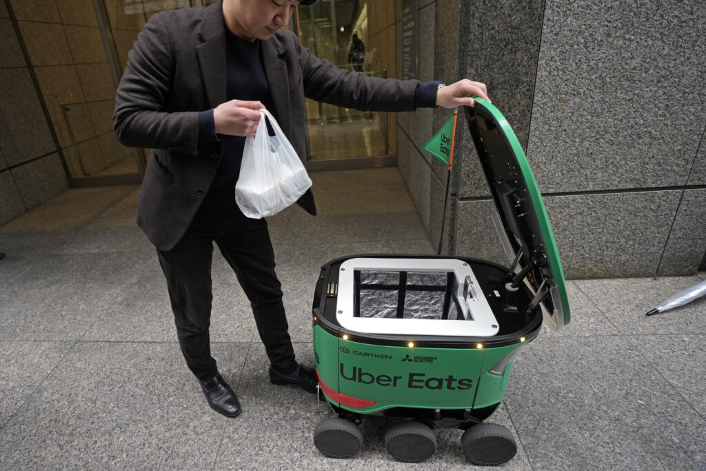A staff receives his order from the container of an Uber Eats food delivery robot during its demonstration for media in Tokyo, Japan, Tuesday, March 5, 2024. Uber Eats Japan plans to launch the robot delivery service in a neighborhood in Tokyo, on Wednesday. (AP Photo/Shuji Kajiyama)