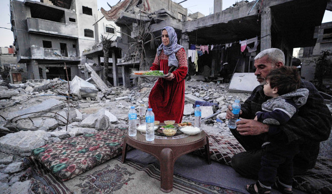 The Palestinian Al-Naji family eats an iftar meal, the breaking of fast, amidst the ruins of their family house, on the first day of the Muslim holy fasting month of Ramadan, in Deir el-Balah in the central Gaza Strip on March 11, 2024, amid ongoing battles between Israel and the militant group Hamas. (AFP)