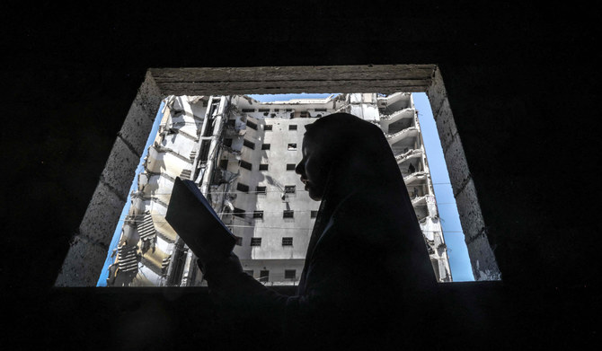 A Palestinian girl reads the Koran, Islam's holy book, on the second day of the of the Muslim fasting month of Ramadan, at home near a window opening on a destroyed building due to Israeli bombardment in Rafah, in the southern Gaza Strip on March 12, 2024, amid ongoing battles between Israel and the militant group Hamas. (AFP)