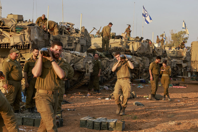 Israeli soldiers carry heavy shells past battle tanks deployed at a position along the border with the Gaza Strip and southern Israel as they pursue Hamas militants in Gaza. (AFP)