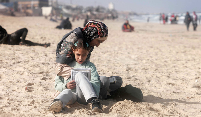 A Palestinian woman and a girl sit along a beach adjoining a makeshift camp for displaced people in Rafah in the southern Gaza Strip on March 30, 2024, amid the ongoing conflict between Israel and the militant group Hamas. (AFP)