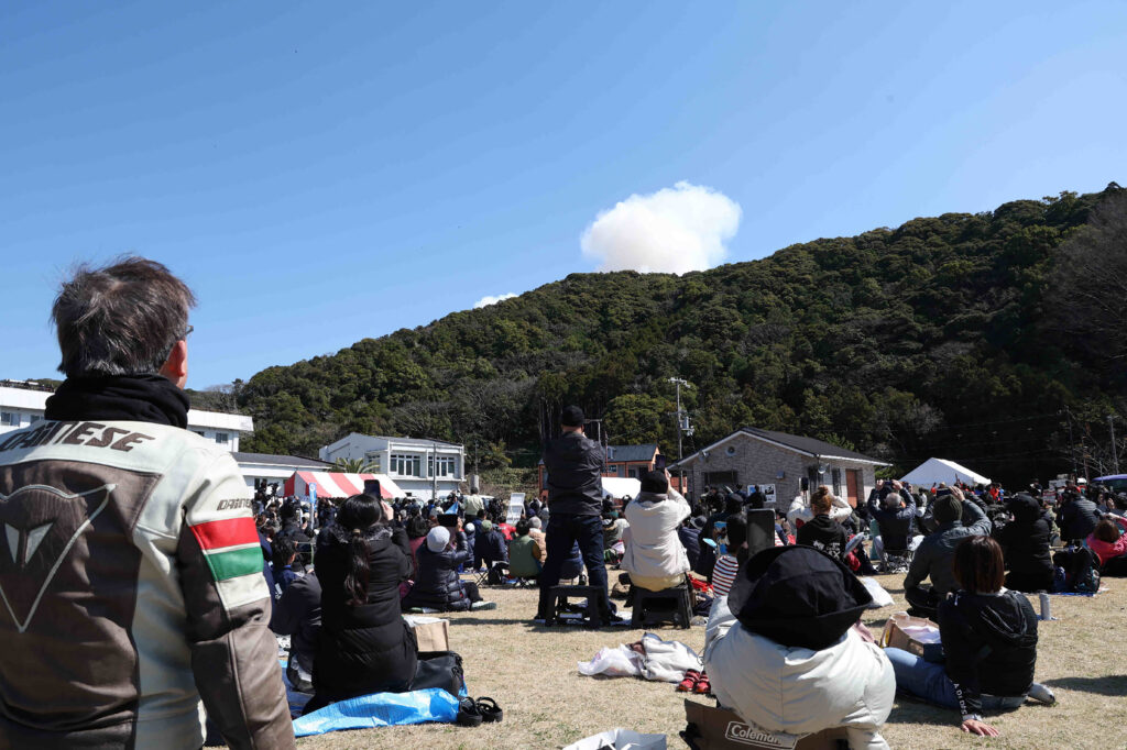 Visitors look on as smoke rises from behind a hill after a small rocket by Tokyo-based startup Space One exploded upon take-off, at the Spaceport Kili site in Kushimoto, Wakayama prefecture, on March 13, 2024. (AFP)