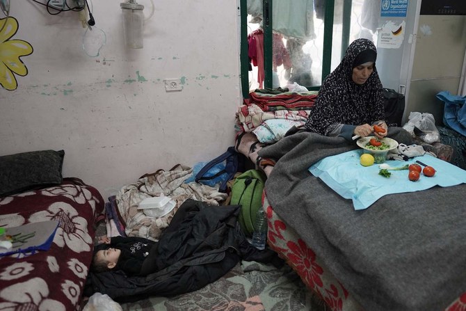 A Palestinian woman cuts vegetables near a sleeping boy at the Shuhada Al-Aqsa Hospital in Deir El-Balah in the central Gaza Strip on April 3, 2024. (AFP)