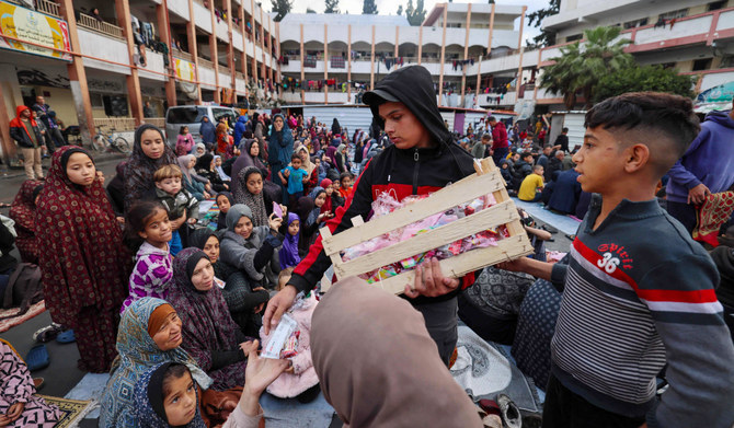 A boy distributes sweets to displaced Palestinians as they attend a special morning prayer to start the Eid al-Fitr festival, marking the end of the holy month of Ramadan, at a school-turned-shelter in Rafah, southern Gaza Strip, on April 10, 2024, amid the ongoing conflict between Israel and the militant group Hamas. (AFP)