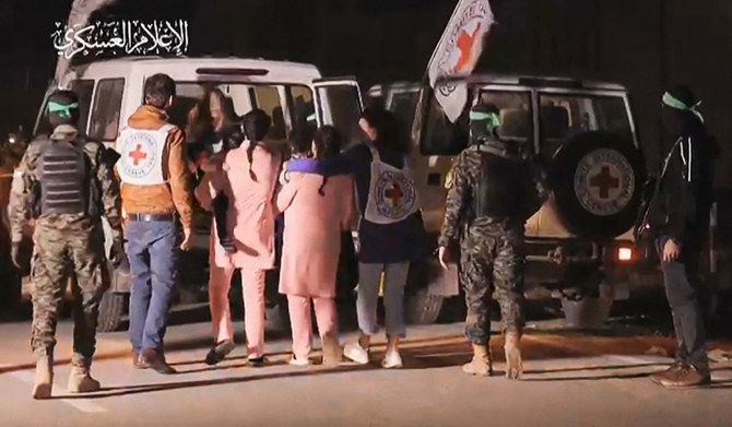 Hamas fighters accompanying newly released Israeli hostages (in pink) to a Red Cross vehicle, in the Gaza Strip on November 27, 2023. (AFP)