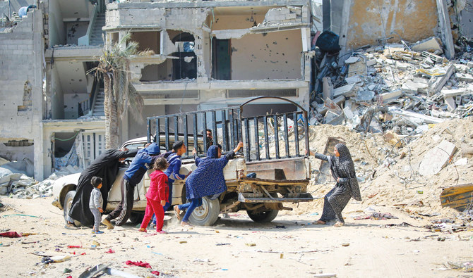 People move a car next to buildings destroyed by Israeli bombardment in Khan Younis, southern Gaza Strip, on Tuesday as fighting continues between Israel and the Palestinian group Hamas. (AFP)