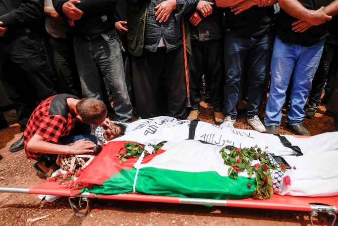 A child kneels over the bodies of two Palestinian men, reportedly killed during an Israeli settlers’ attack on the village of Aqraba in the Israeli-occupied West Bank, during their funeral procession on April 20, 2024. (AFP)