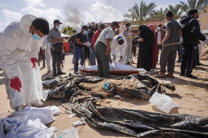Palestinian health workers stand next to unearthed bodies buried by Israeli forces in Nasser hospital compound in Khan Younis in the southern Gaza Strip on April 21, 2024. (AFP)