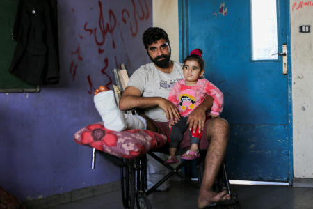 Displaced Palestinian Hamza Abu Alkas, who was wounded while trying to receive aid, holds his daughter as he sits in a classroom at an UNRWA school where they shelter, amid the ongoing conflict between Israel and Hamas, in Gaza City, April 3, 2024. (Reuters)