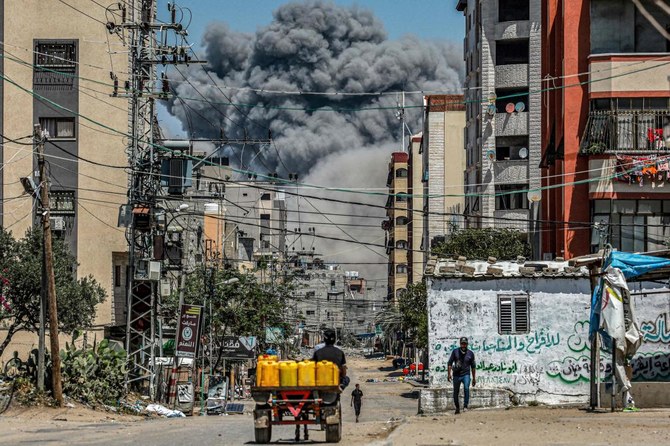 A cloud of smoke erupts down the road as a man drives an animal-drawn cart loaded with jerrycans in Nuseirat in the central Gaza Strip on April 17, 2024. (AFP)