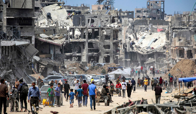 People move past destroyed buildings along a street in Khan Yunis in the southern Gaza Strip on May 14, 2024 amid the ongoing conflict in the Palestinian territory between Israel and Hamas. (AFP)