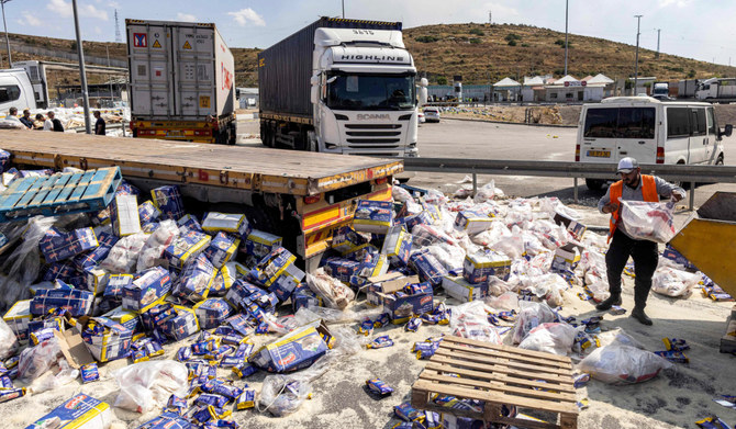 A worker clears spilled goods away from damaged trailer trucks that were carrying humanitarian aid supplies on the Israeli side of the Tarqumiyah crossing with the occupied West Bank on May 13, 2024, after they were vandalised by other activists to protest against aid being sent to the Gaza Strip. (AFP)