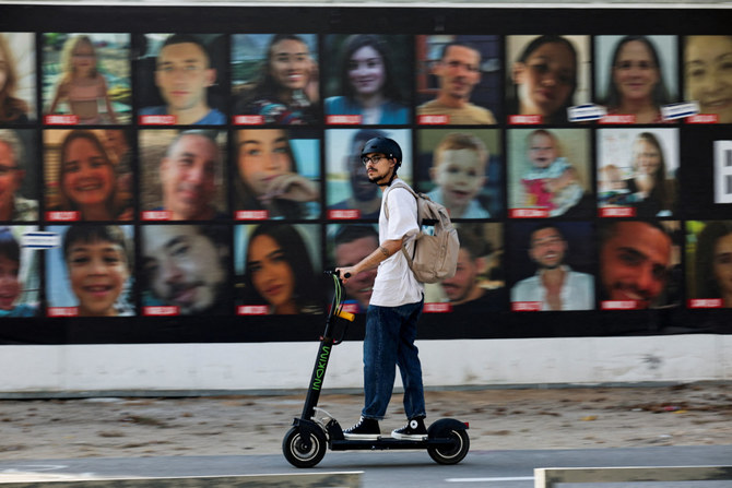 A man rides a scooter in Tel Aviv, past pictures of hostages kidnapped during the deadly October 7 attack by the Palestinian Islamist group Hamas. (REUTERS)