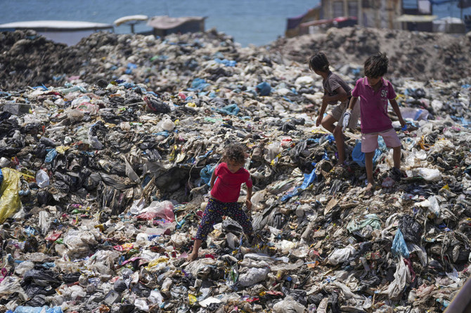Children trudge through water contaminated with sewage and scale growing mounds of garbage in Gaza’s tent camps for displaced families. (AP)