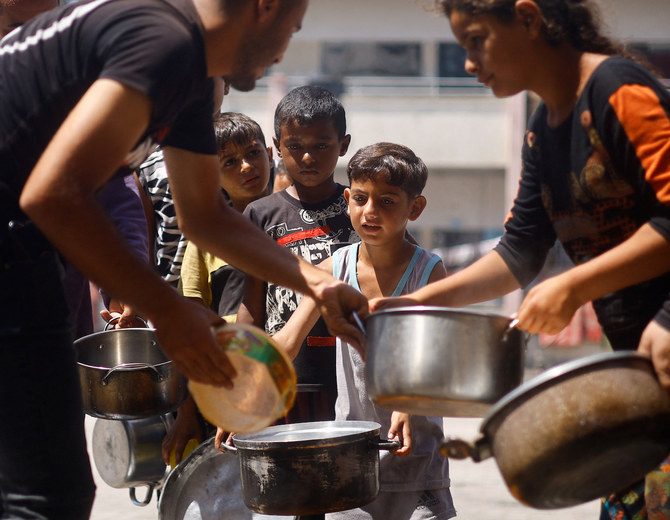 Palestinian children gather to receive food cooked by a charity kitchen, amid food scarcity in Khan Younis in the southern Gaza Strip, June 26, 2024. (Reuters)