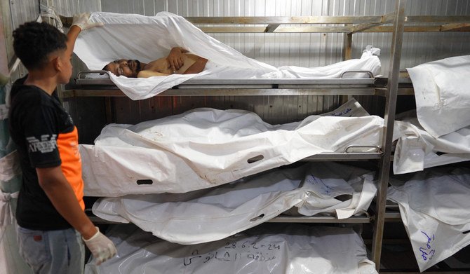 A Palestinian youth who works with his father at the morgue uncovers the body of one of several unidentified people killed recently amid the continuing conflict between Israel and Hamas in the southern Gaza Strip, at the Nasser hopsital in Khan Yunis on July 5, 2024. (AFP)