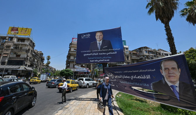 People walk past electoral campaign posters ahead of parliament elections in Damascus, on July 10, 2024. (AFP)