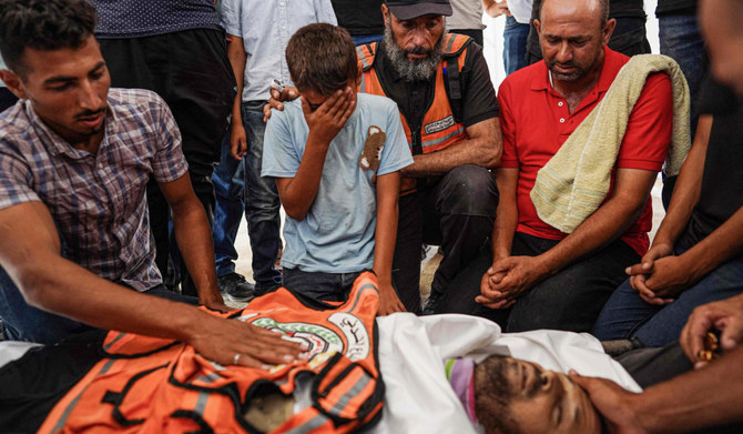 Relatives and Palestinian Civil Defence members mourn by the body of their colleague Bilal Ramadan Farhan, 42, who died of injuries sustained in Israeli bombing of al-Mawasi area two days earlier, while comforting his son Ahmed, 11, during his funeral at Nasser hospital in Khan Yunis on July 15, 2024, amid the ongoing conflict between Israel and the Palestinian Hamas militant group. (AFP)