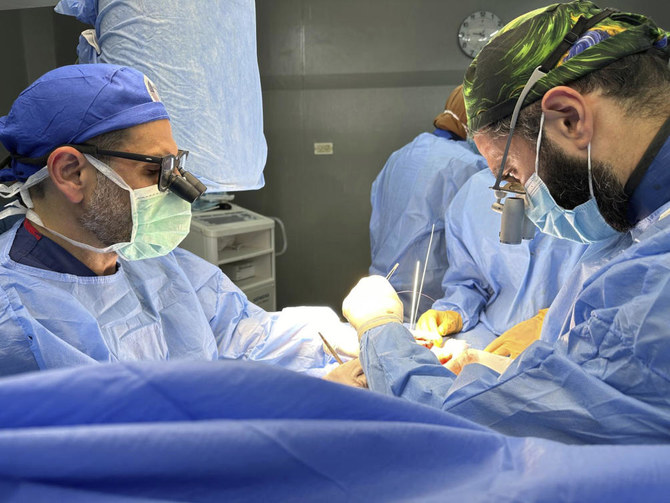 Dr. Adam Hamawy, left, a former US Army combat plastic surgeon, and Dr. Mohammed Tahir, a British surgeon, perform surgery on mangled hand from a blast injury at the European General Hospital, in Khan Younis, Gaza. (Adam Hamawy via AP)
