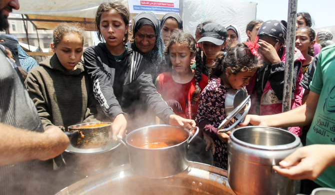 Palestinians gather to receive food cooked by a charity kitchen, amid shortages of aid supplies, as the conflict between Israel and Hamas continues, in Khan Younis, in the southern Gaza Strip, June 19, 2024. (REUTERS)