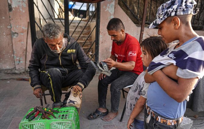 Palestinians wait for a cobbler to repair their shoes in the city of Khan Yunis, in the southern Gaza Strip on July 5, 2024. (AFP)