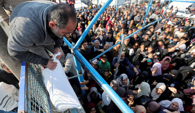 A Palestinian man holds a flour bag as others wait to receive theirs from the United Nations Relief and Works Agency (UNRWA) during a temporary truce between Hamas and Israel, in Khan Younis in the southern Gaza Strip, November 29, 2023. (REUTERS)