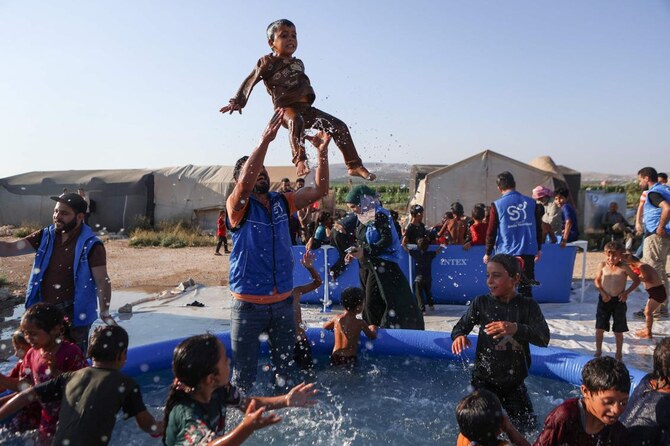 A volunteer throws a child into the air as displaced Syrian children play in a mobile swimming pool set up by the Smile Younited charity organisation, during the sweltering summer heat in the Kafr Naseh camp, in the rebel-held part of Aleppo province. (AFP)