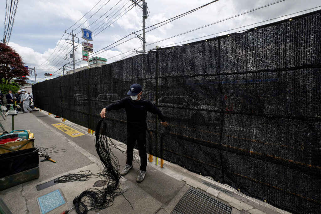 A worker finishes the barrier installation work to block the sight of Japan's Mount Fuji emerging from behind a convenience store to deter badly behaved tourists, in the town of Fujikawaguchiko, Yamanashi prefecture on May 21, 2024. (AFP)