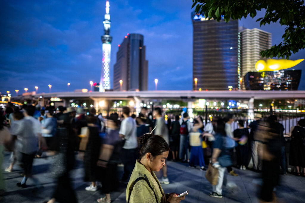 People gather along the Sumida River promenade to watch the