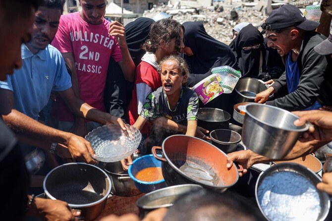 A child reacts as people gather to receive meals during food distribution from a kitchen in the Bureij camp for Palestinian refugees in the central Gaza Strip on August 21, 2024. (AFP)