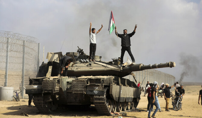 Palestinians wave their national flag and celebrate by a destroyed Israeli tank at the southern Gaza Strip fence east of Khan Younis on Saturday, Oct. 7, 2023. (AP)