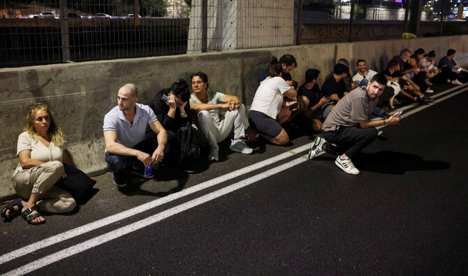 People take cover by the side of a road as a siren sound, after Iran fired a salvo of ballistic missiles at Israel, in Tel Aviv, Israel. (Reuters)