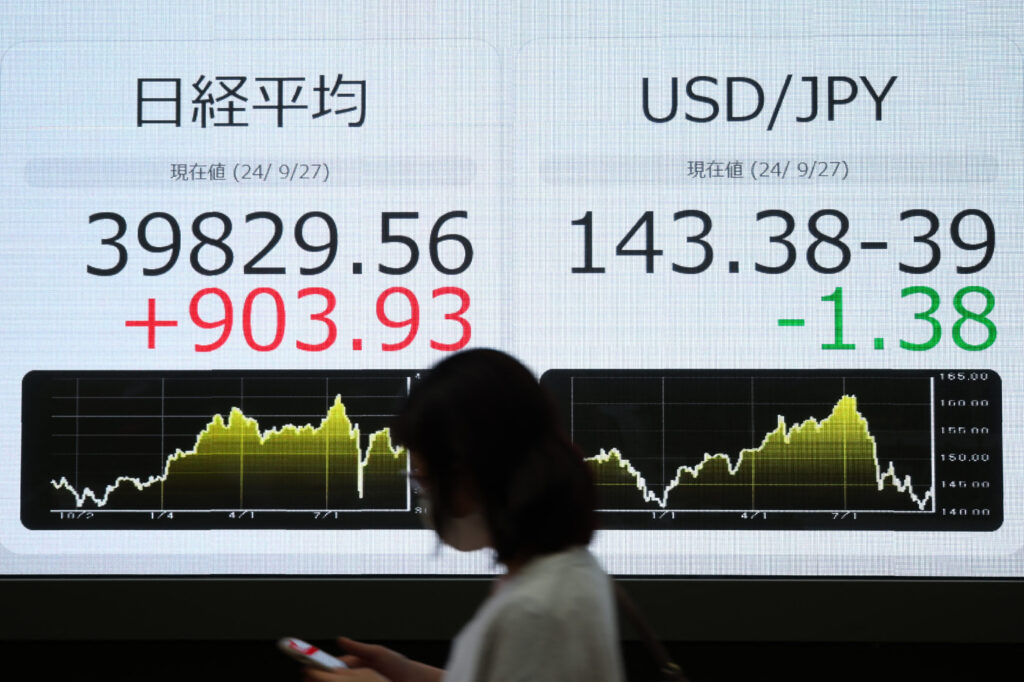 A pedestrian walks past an electronic board showing the closing numbers on the Tokyo Stock Exchange (L) and the Japanese yen rate against the US dollar (R), along a street in Tokyo on September 27, 2024. (AFP)