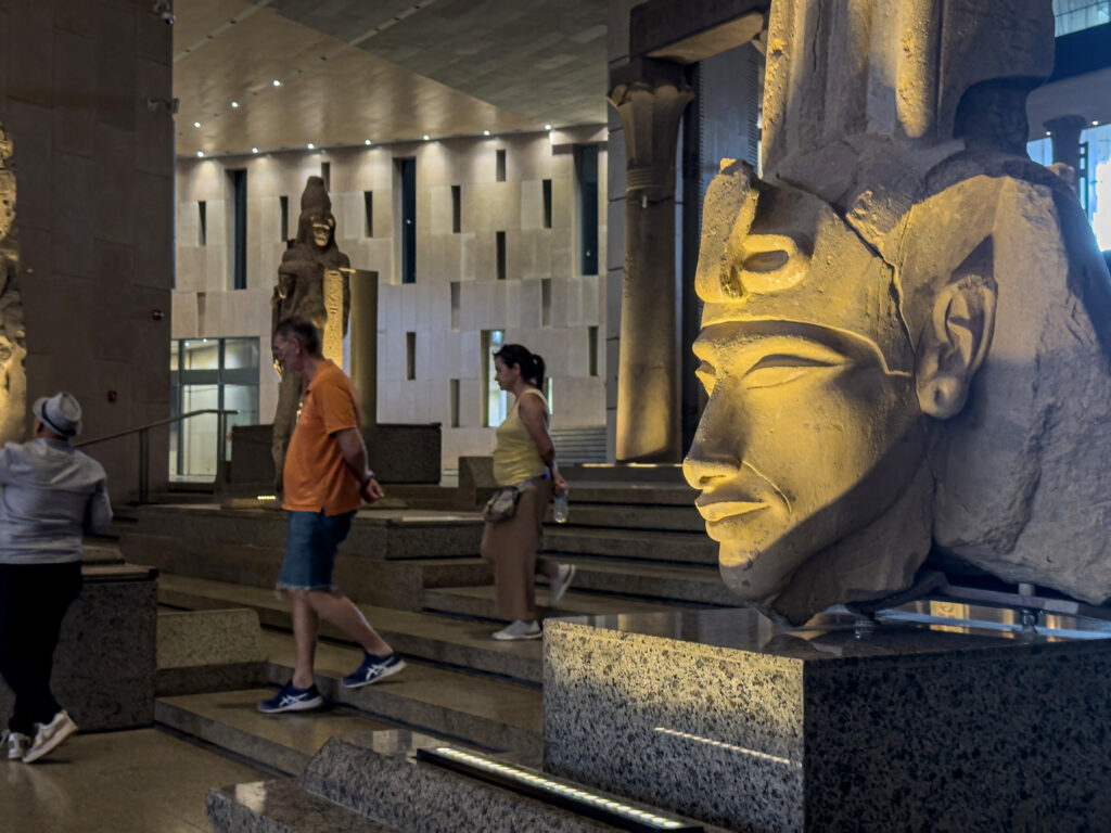 This picture shows on October 15, 2024, visitors walking past a fragment of an ancient Egyptian colossal statue of the 18th dynasty king Akhenaten (also known as Amenhotep IV - 1353-1334 BC) along the Grand Staircase at the Grand Egyptian Museum in Giza during the trial operation of the Grand Egyptian Museum. (AFP)