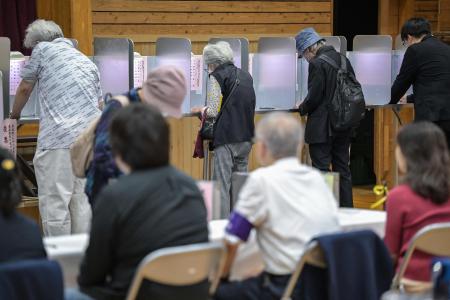 Officials look on as people vote during the general election at a polling station set up at a local school in Tokyo on October 27, 2024. (AFP)