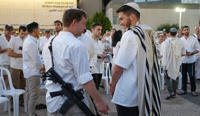 An armed man talks to another ahead of evening prayers during the Jewish holiday of Yom Kippur in Tel Aviv on October 11, 2024. Yom Kippur or the Day of Atonement, which starts at sunset on October 11, is the most sacred day of the Jewish calendar. (AFP)